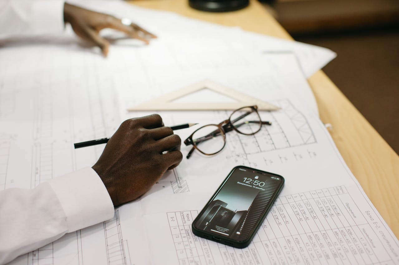 Close-up of an architect drafting on papers with a smartphone and glasses on a desk.